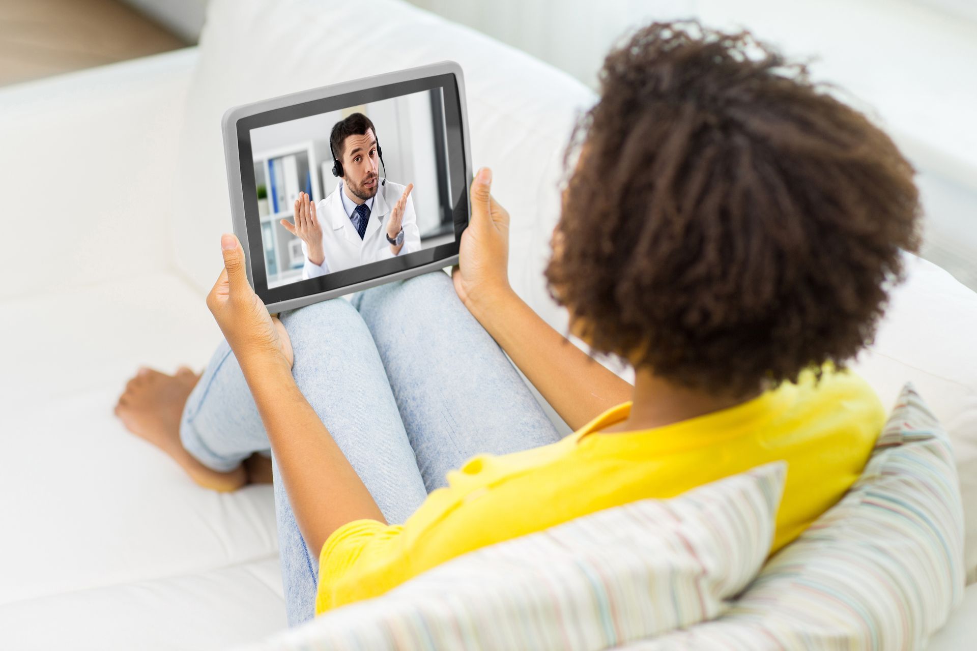 Person on a couch video chatting on a tablet with a doctor on screen