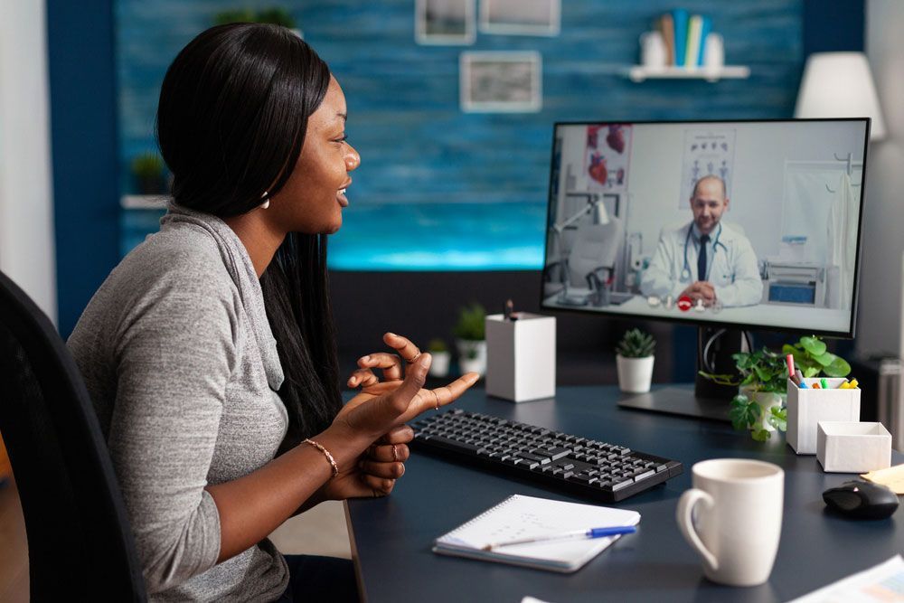 Woman in teleconference with a doctor at a desk, smiling.