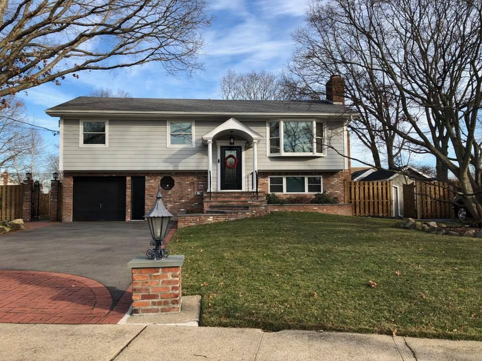 A two-story split-level home with grey siding, a brick lower level, a black front door, and a paved driveway.