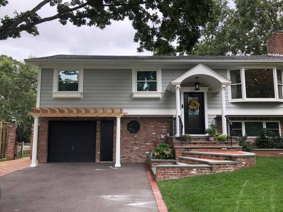 A two-story house with gray horizontal siding, a brick lower level, a black garage door, and a front porch with pillars.