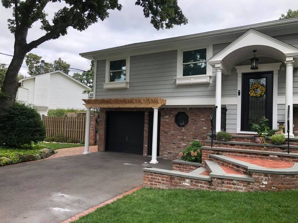 A split-level home with grey horizontal siding, a brick lower level, a black garage door, and stone entry stairs.