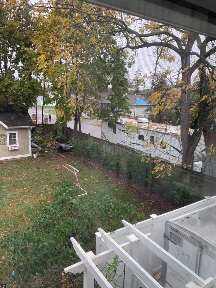 A backyard view from an upper window, showing a lawn, a white trellis, a small house, and a recreational vehicle parked.