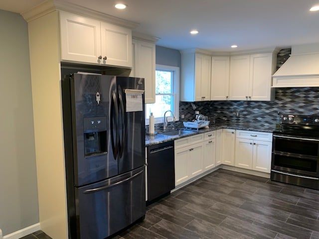 A kitchen with white cabinets, dark stainless steel appliances, a gray mosaic backsplash, and wood-look flooring.