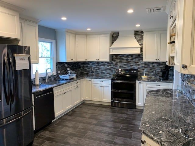 Modern kitchen with white cabinets, dark granite countertops, stainless steel appliances, and a gray tile backsplash.