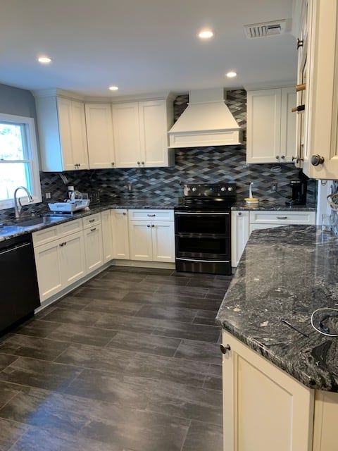 A modern kitchen with white cabinets, dark patterned countertops, a textured gray backsplash, and wood-look tile flooring.
