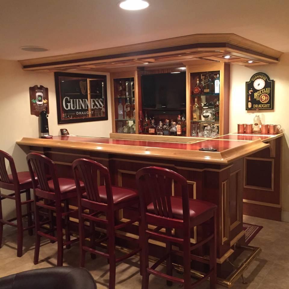 A home bar with wooden cabinetry, red upholstered stools, a Guinness sign, and a recessed back bar with shelves.