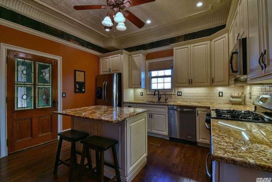 A kitchen with white cabinets, granite countertops, a center island with two stools, and warm orange walls.