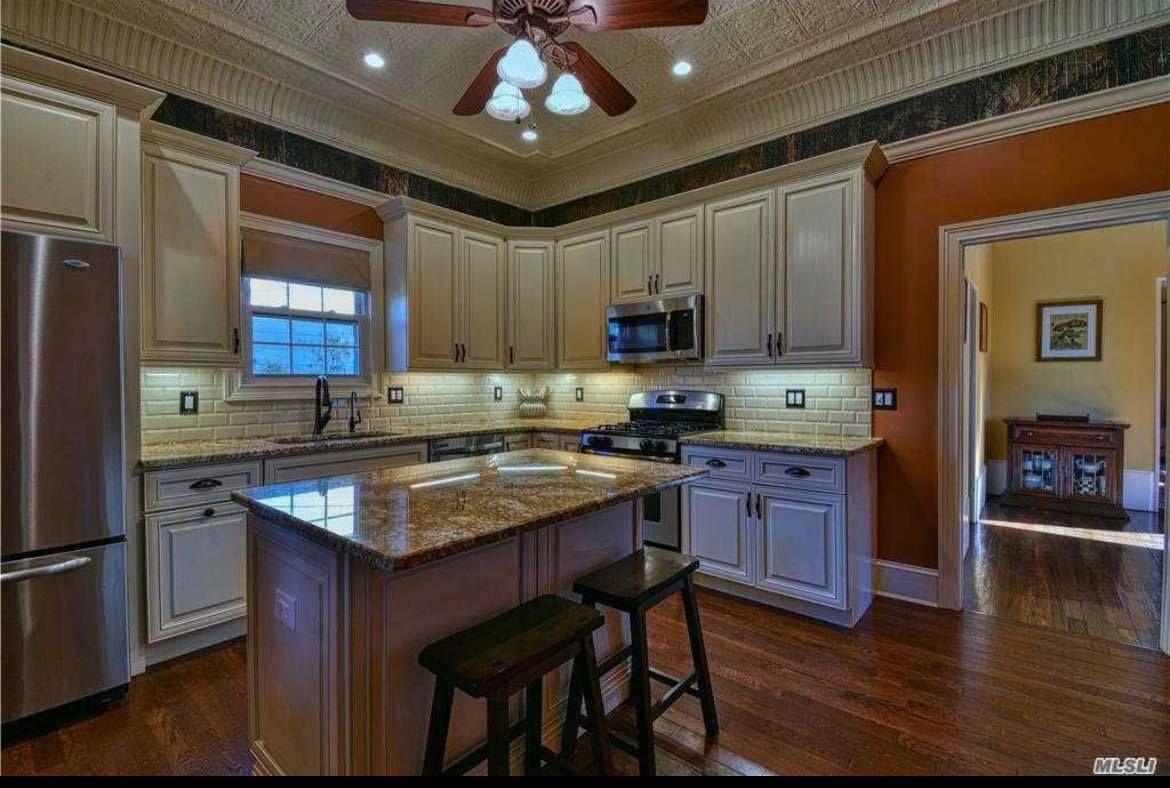 A kitchen with cream cabinets, granite countertops, a center island with two stools, and warm-toned walls.