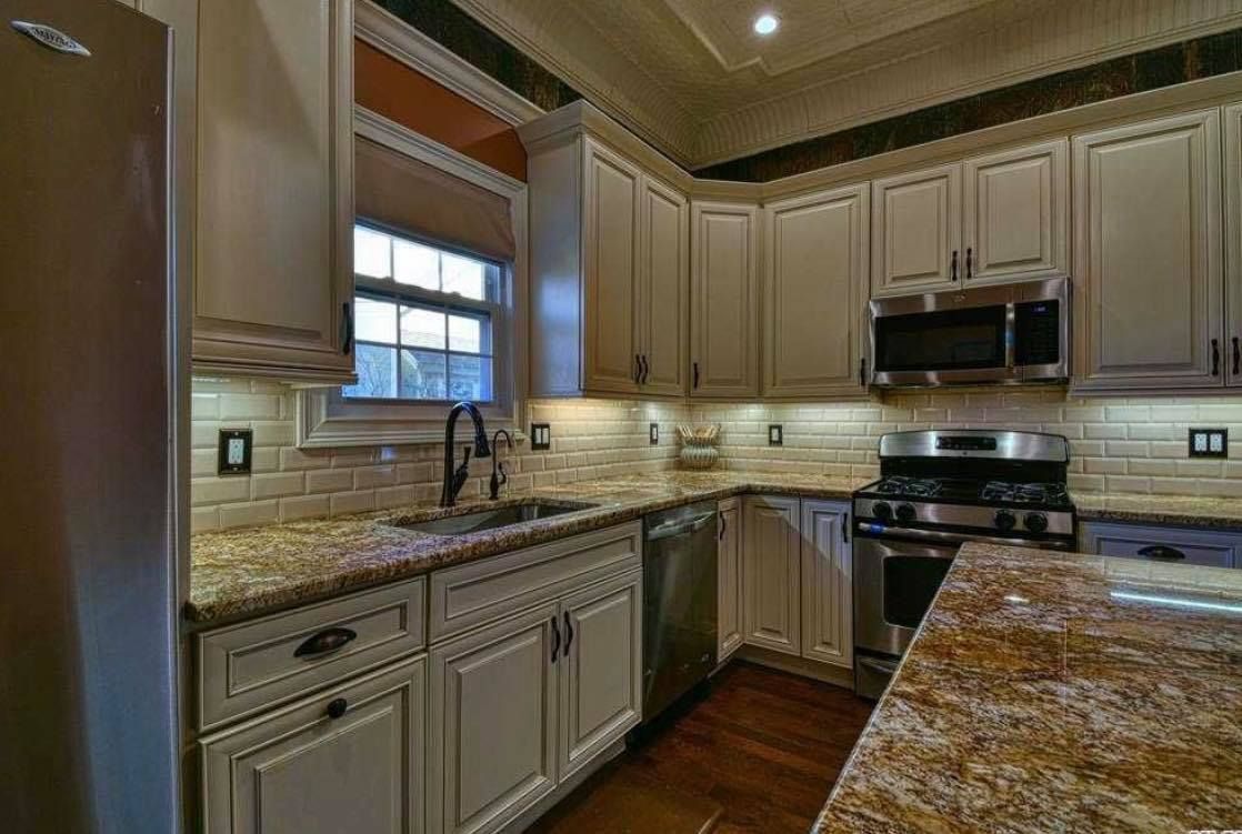 A kitchen with cream-colored cabinets, granite countertops, stainless steel appliances, and a tiled backsplash.