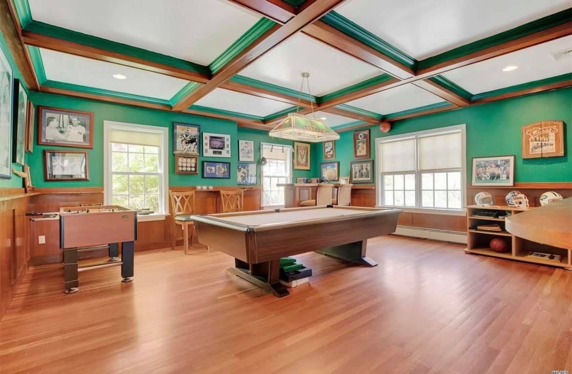 A game room with green walls, hardwood floors, a billiard table, a foosball table, and framed artwork on the walls.