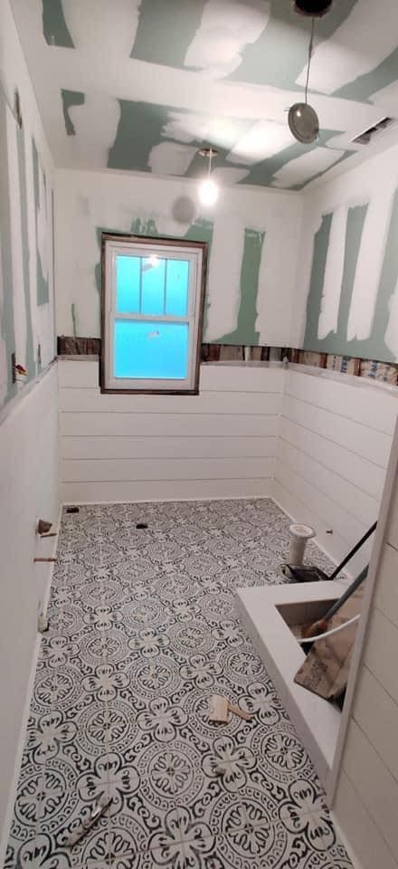 A bathroom under construction with patterned tile flooring, partially installed white shiplap walls, and unfinished drywall.