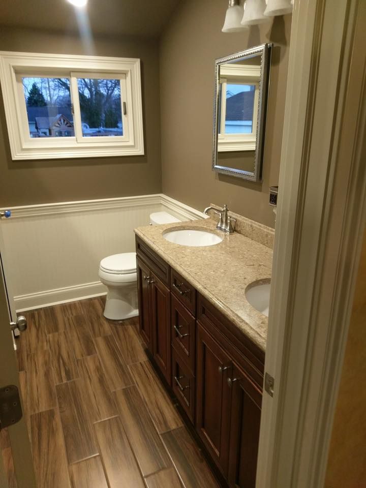 A bathroom with dark wood cabinets, a speckled beige countertop, white toilet, and wood-look tile flooring.