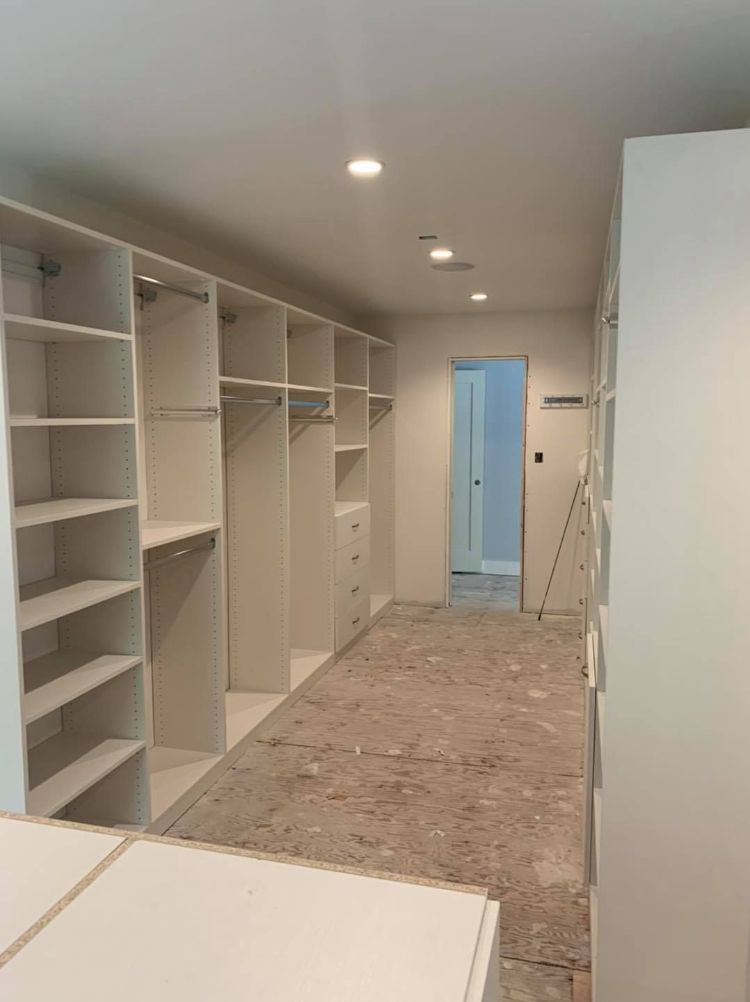 A walk-in closet under construction with white shelving units along the walls and an unfinished floor.