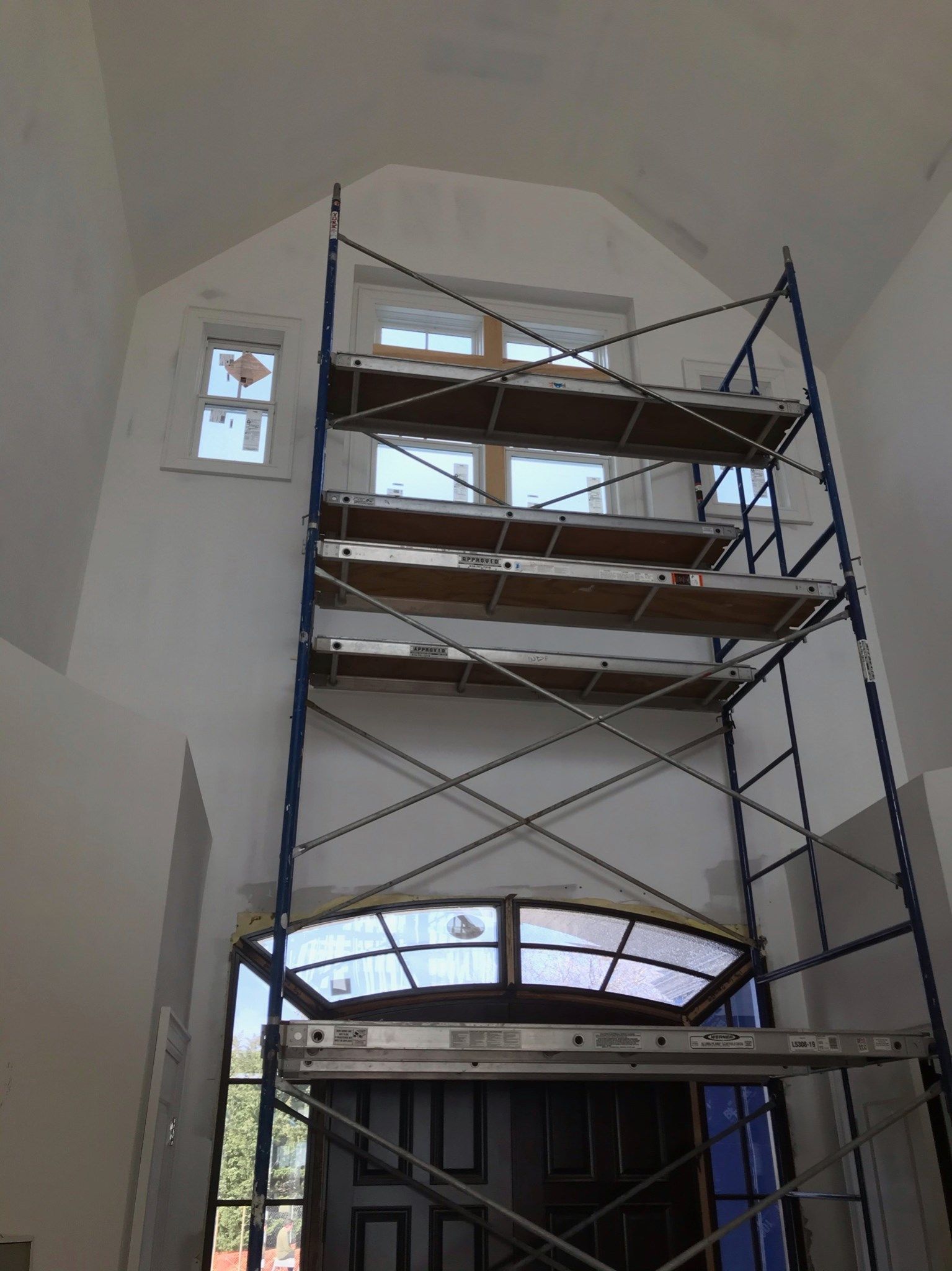 Metal scaffolding towers inside a high-ceilinged room in front of an arched entryway and upper windows.