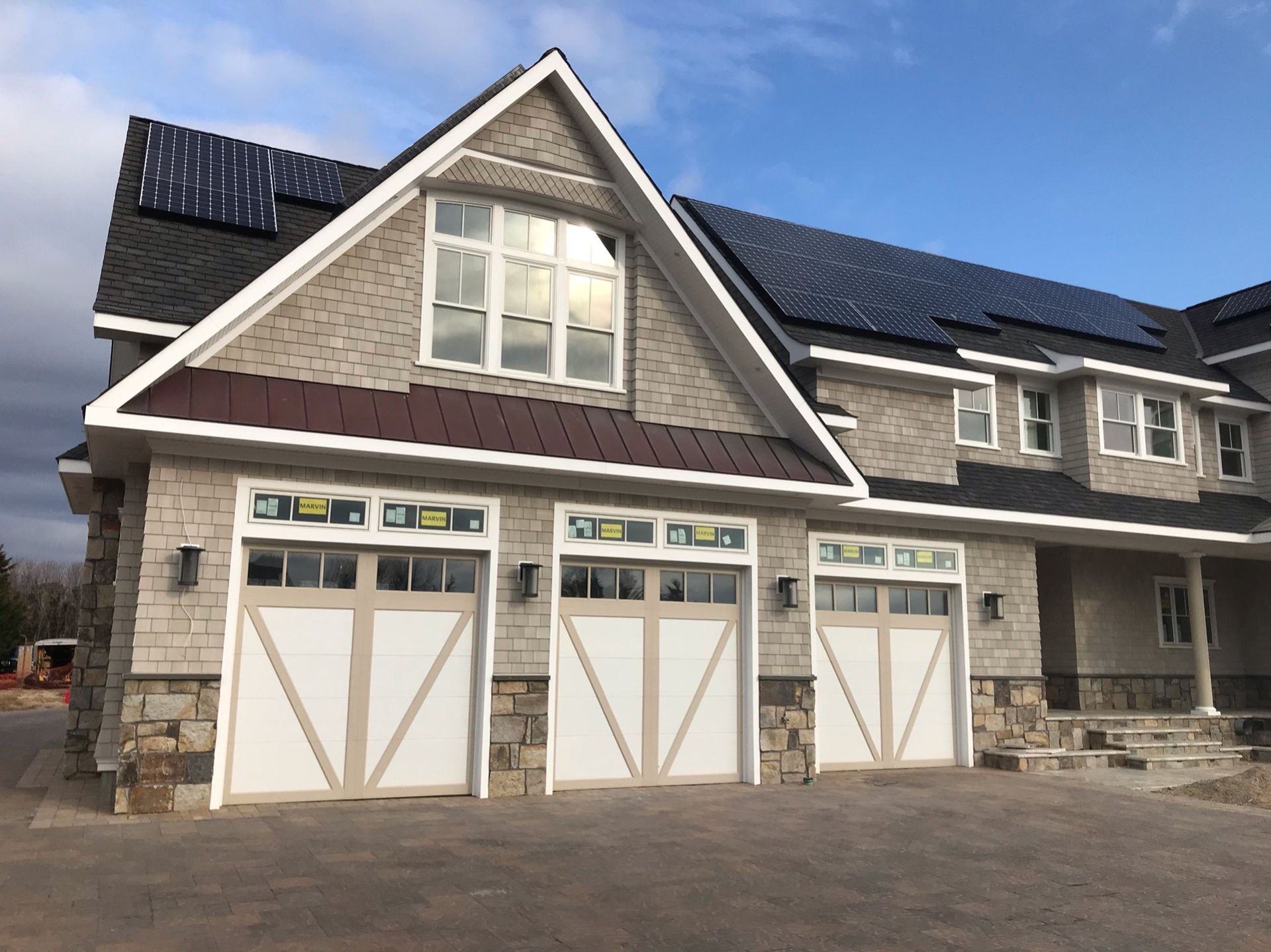 A stone three-car garage house with solar panels on the roof and a concrete driveway on a sunny day.
