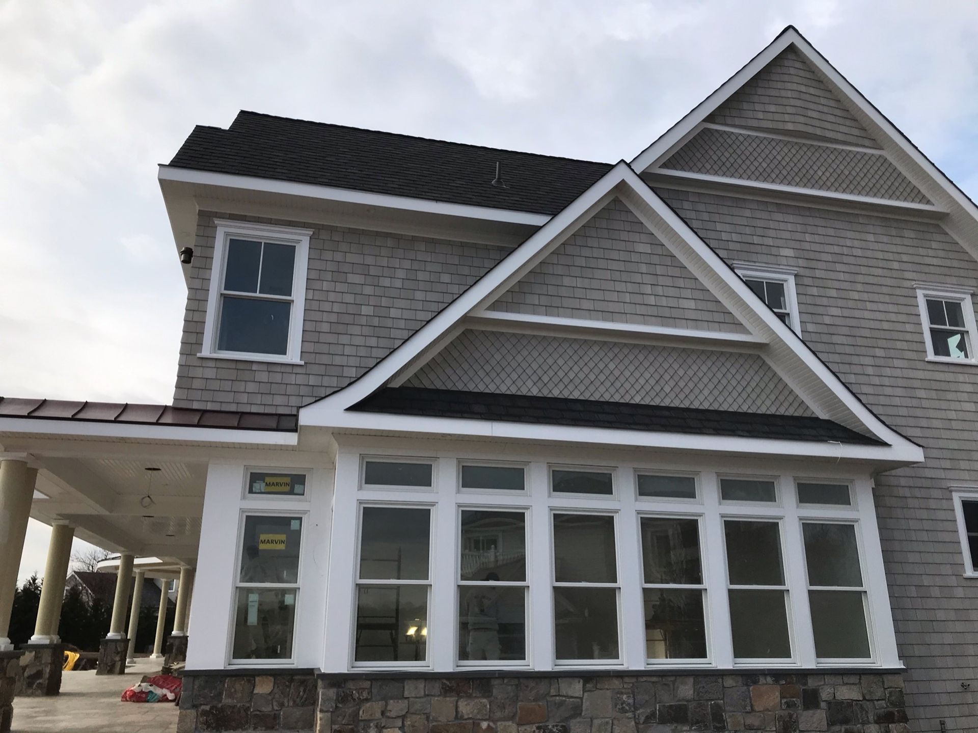 A two-story house with gray stone siding, white window trim, and a porch under a roof section with a triangular gable.