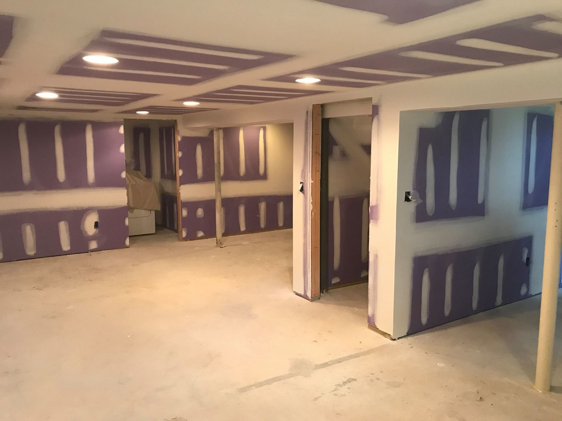 A basement renovation in progress, featuring purple moisture-resistant drywall, taped seams, and recessed lighting.
