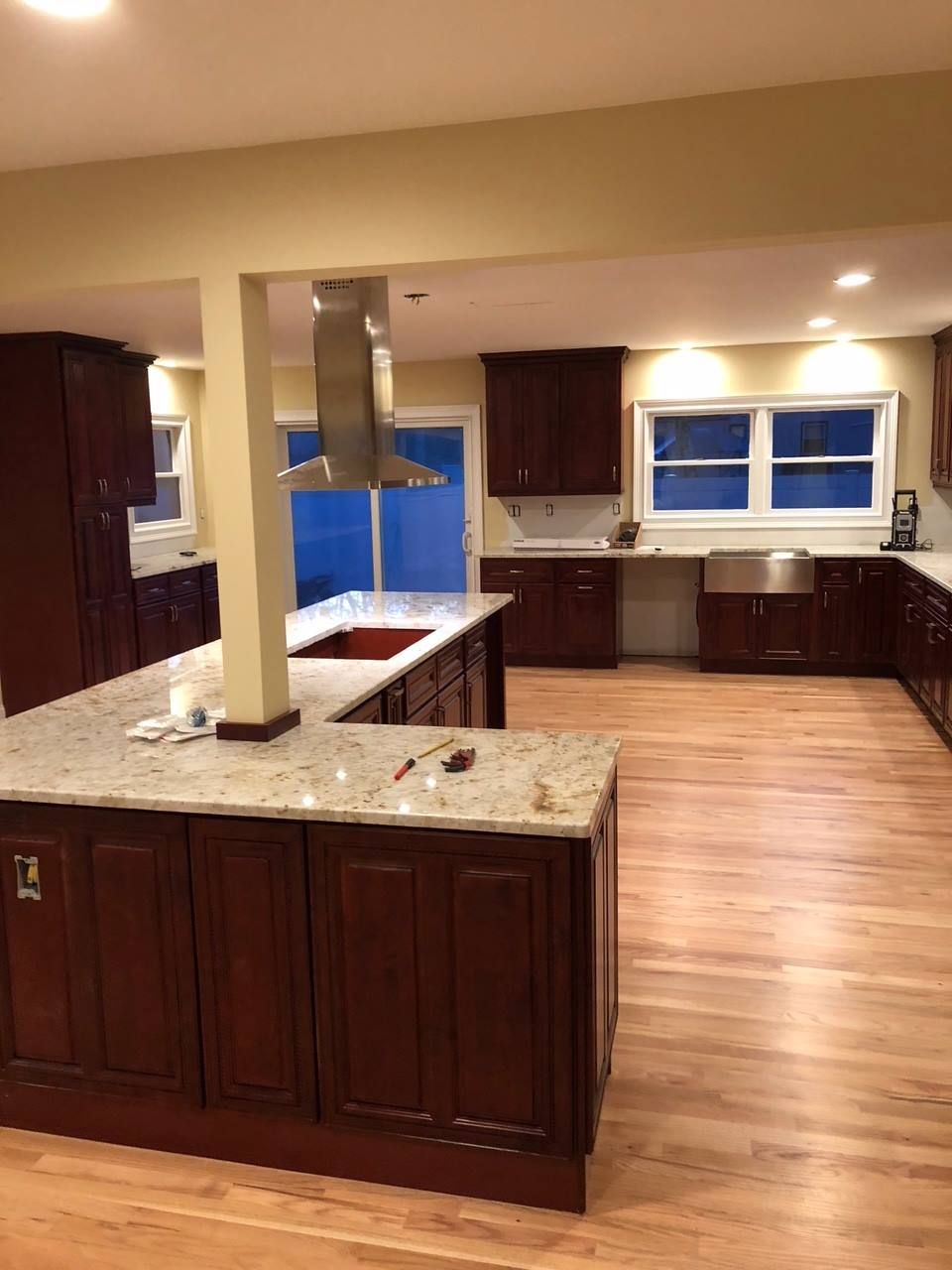A modern kitchen featuring dark wood cabinets, light granite countertops, a central island, and hardwood floors.