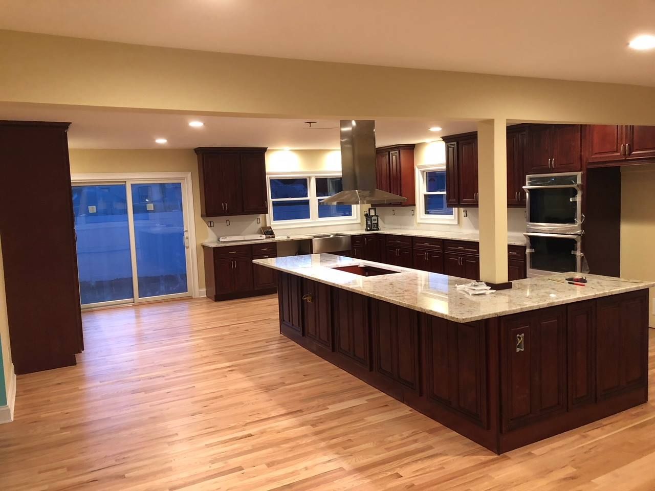 A spacious kitchen featuring dark wood cabinets, a large granite island, stainless steel appliances, and wood flooring.