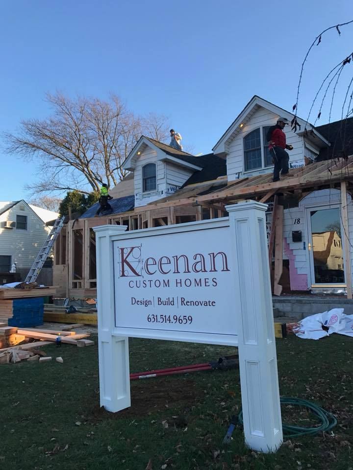 A Keenan Custom Homes sign stands in front of a residential home under renovation with workers on the roof.