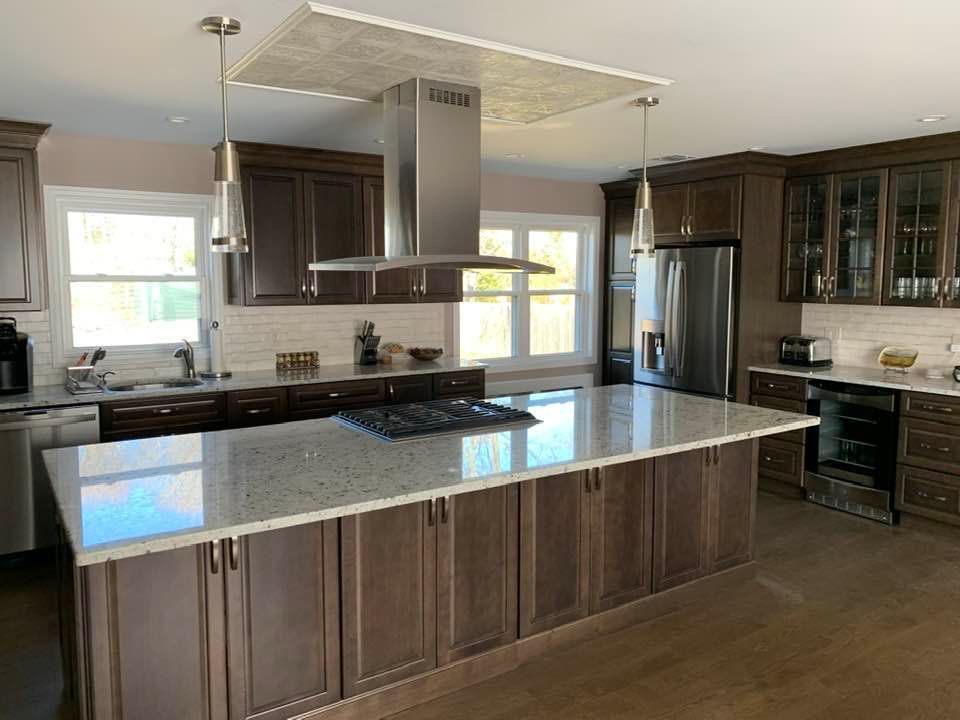 A modern kitchen with dark wooden cabinetry, a large island with a quartz countertop, and a stainless steel range hood.