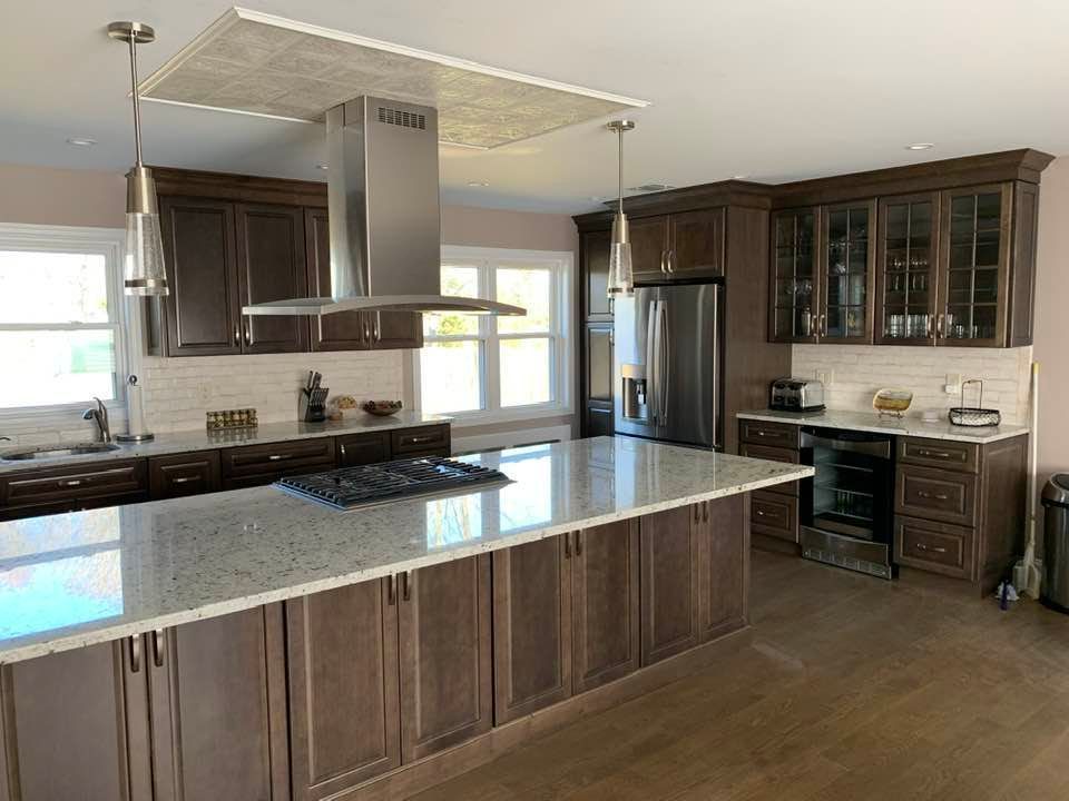 Modern kitchen with dark wood cabinets, a large granite island, stainless steel appliances, and two hanging light fixtures.