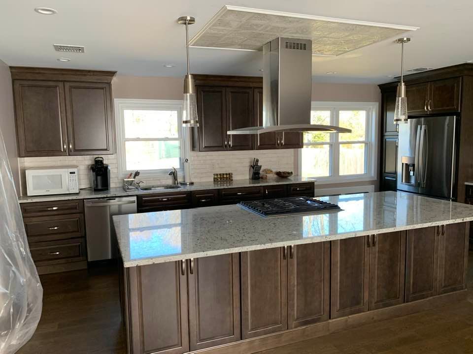Modern kitchen with dark wood cabinetry, a large marble island, stainless steel appliances, and a hanging range hood.