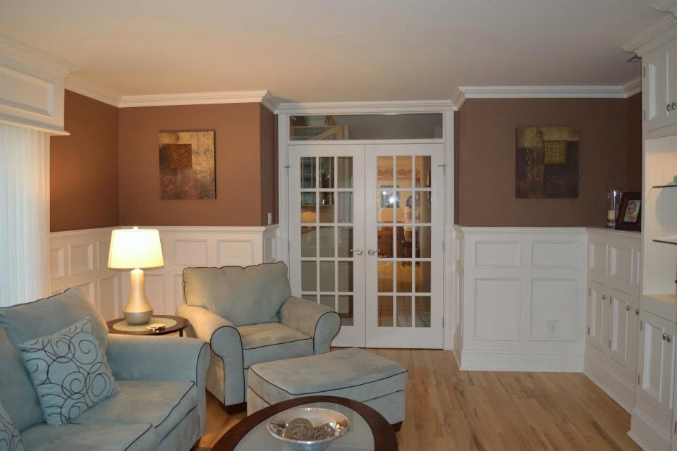 A light blue sofa and chair sit in a room with white wainscoting, brown walls, and French doors leading to another room.