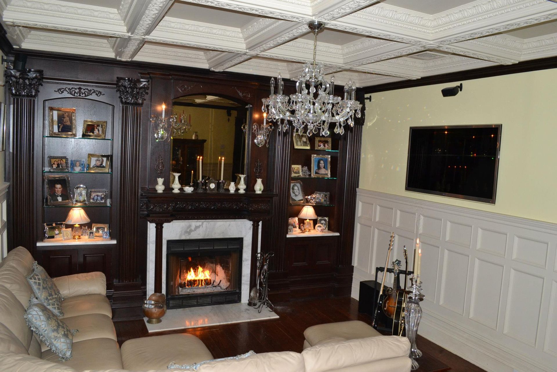 A living room with dark wood shelving around a fireplace, a crystal chandelier, coffered ceiling, and beige sofa.