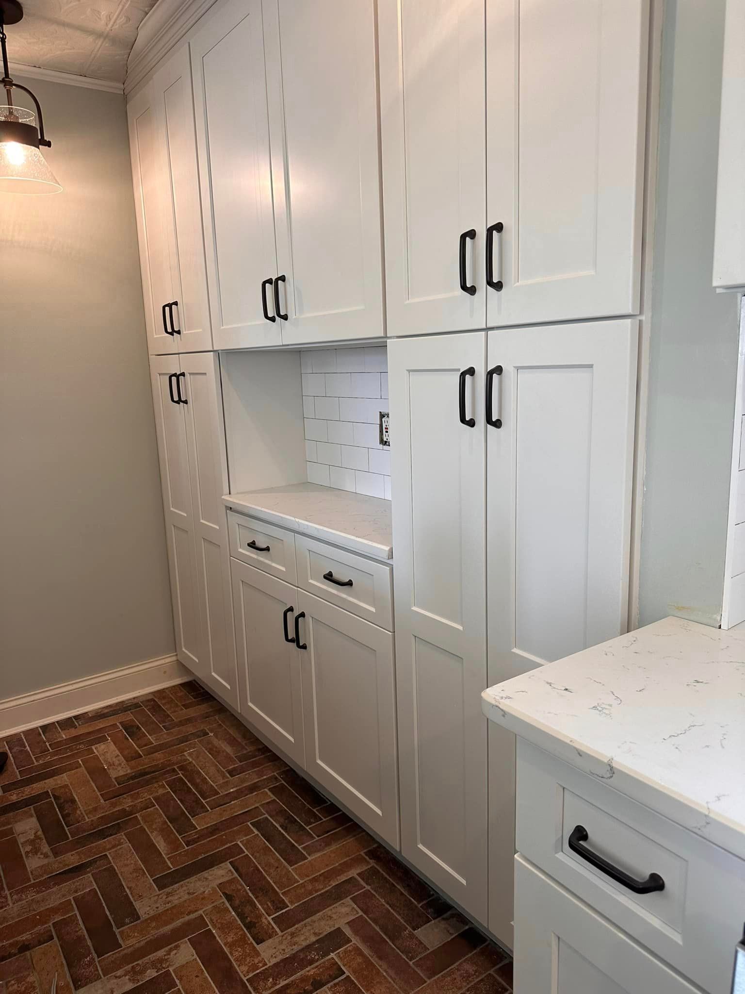 White kitchen cabinets with black handles, a light countertop, and a patterned brick-style tile floor.