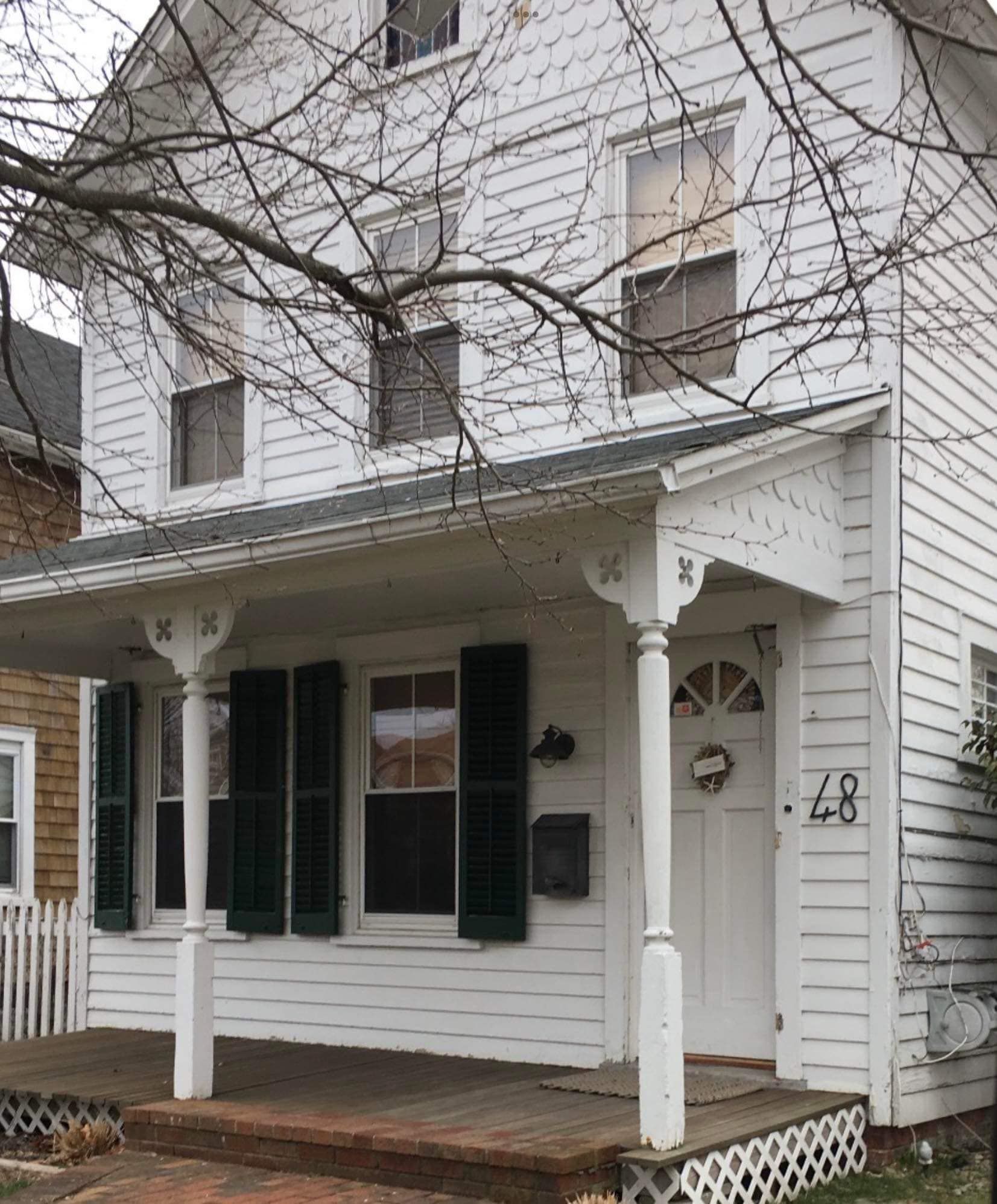 A two-story, white wood-sided house with a front porch, dark shutters, and the number 48 on the wall.