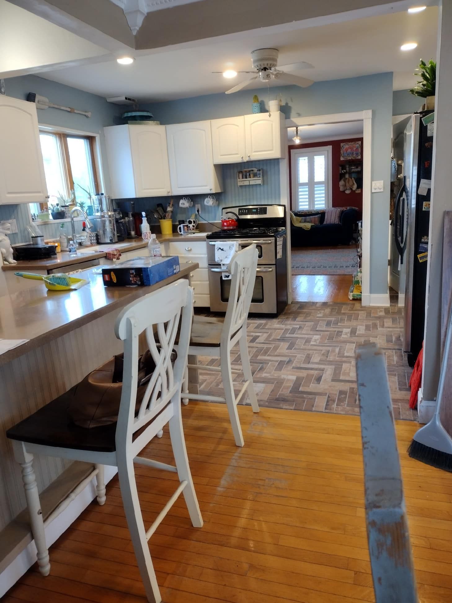 A bright kitchen features white cabinets, a light wood floor, a breakfast bar with two white chairs, and a stove.