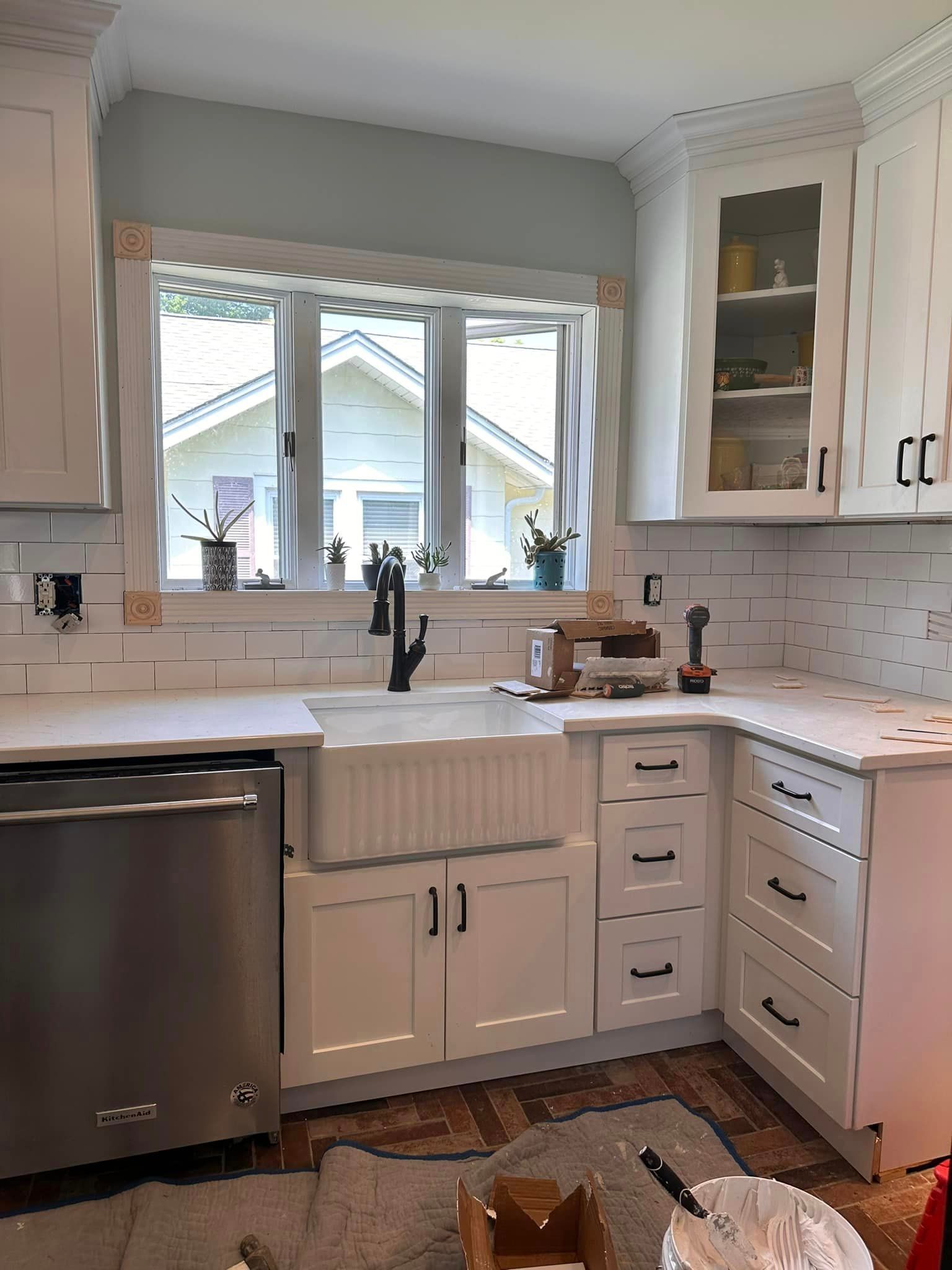A kitchen featuring white cabinets, a farmhouse sink, stainless steel dishwasher, and a subway tile backsplash.