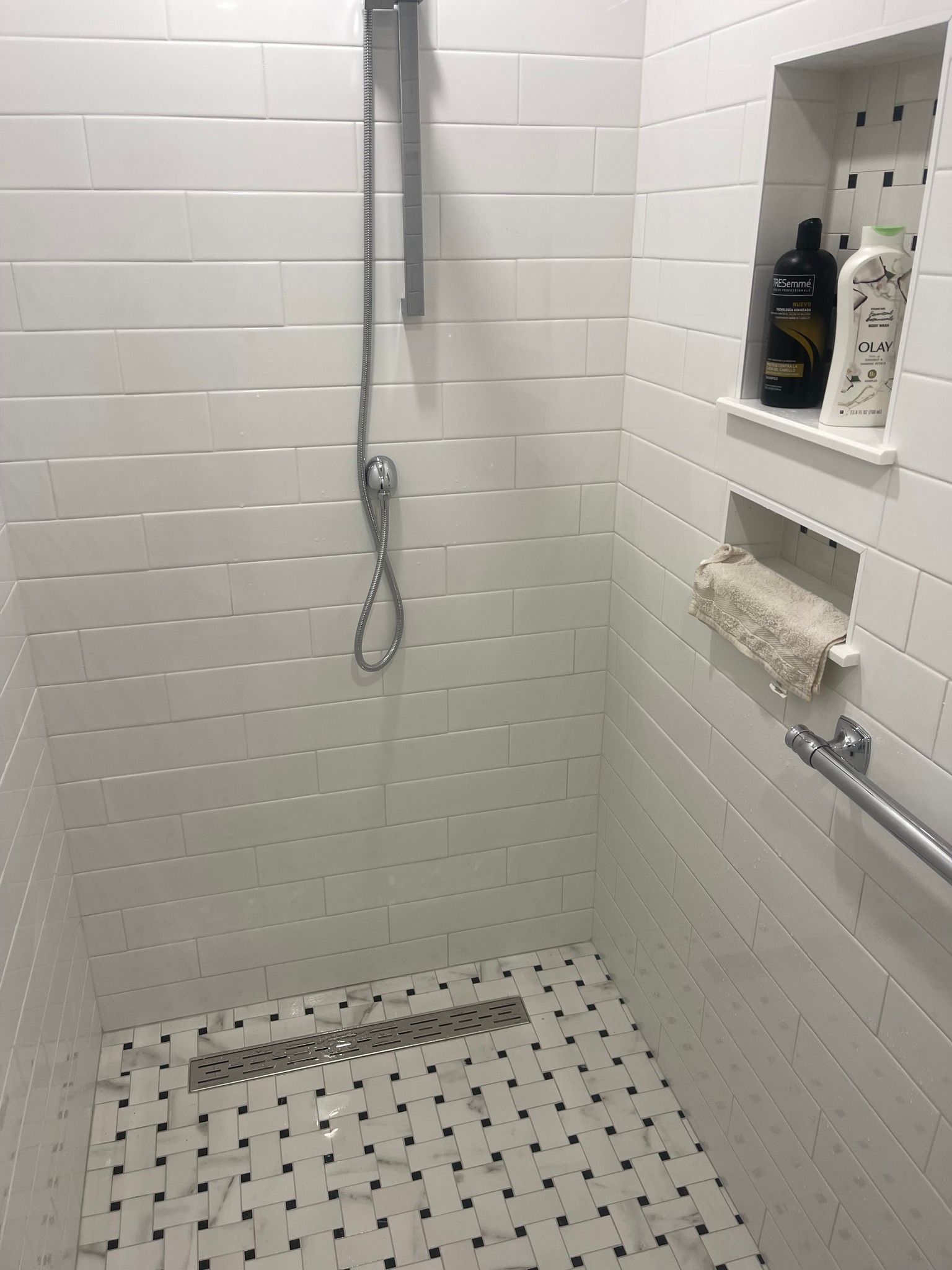 A modern walk-in shower with white subway tile walls, a patterned tile floor, a shower head, and two storage niches.
