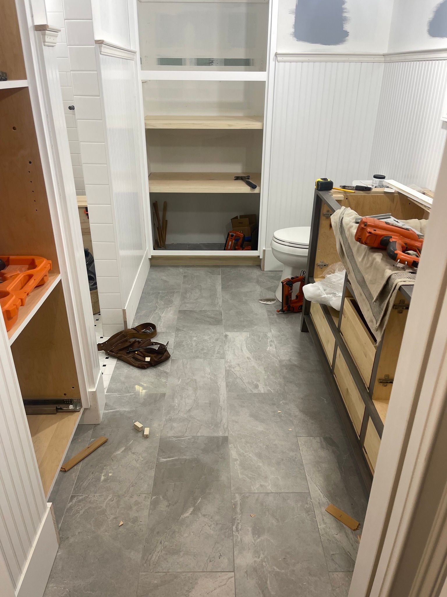 A bathroom under construction with gray tiled flooring, white beadboard wainscoting, built-in shelving, and a vanity.