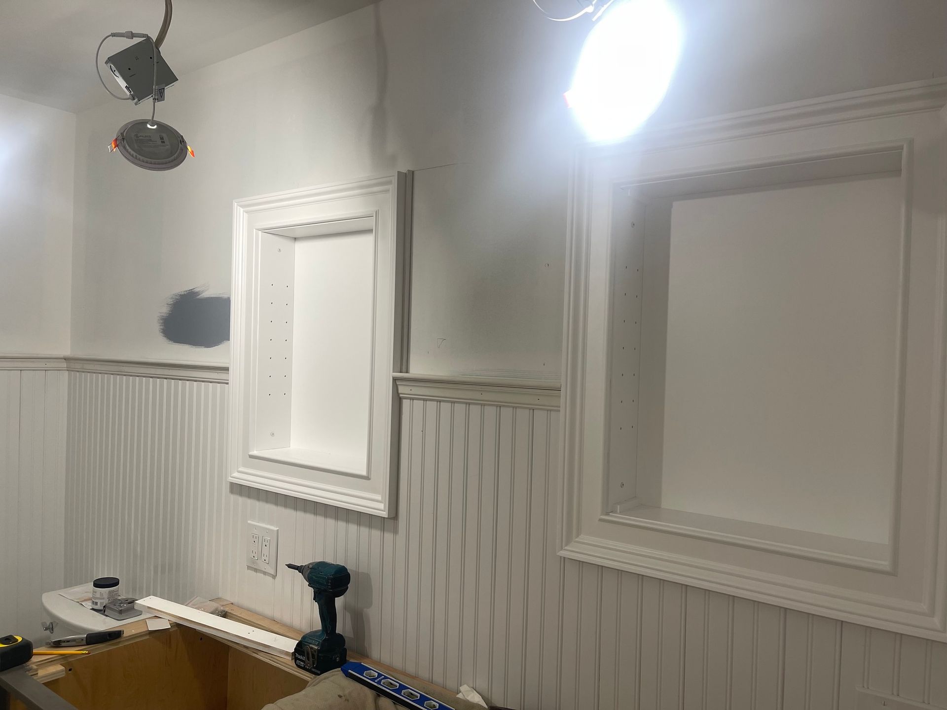 A room under construction with white beaded-board wainscoting and two rectangular recessed wall niches installed.