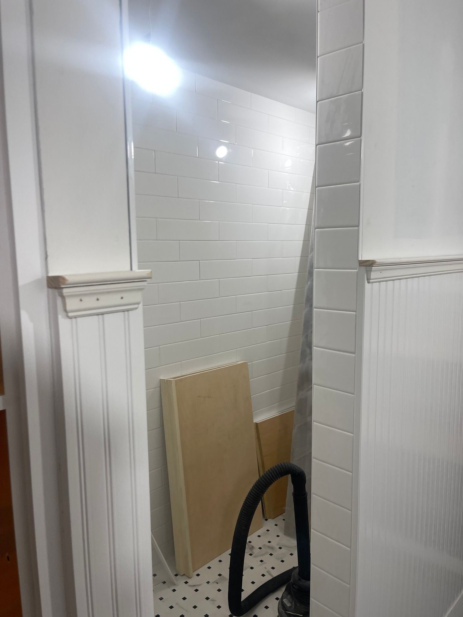 A bathroom under renovation featuring white subway tile walls, a black and white tiled floor, and a wooden trim detail.