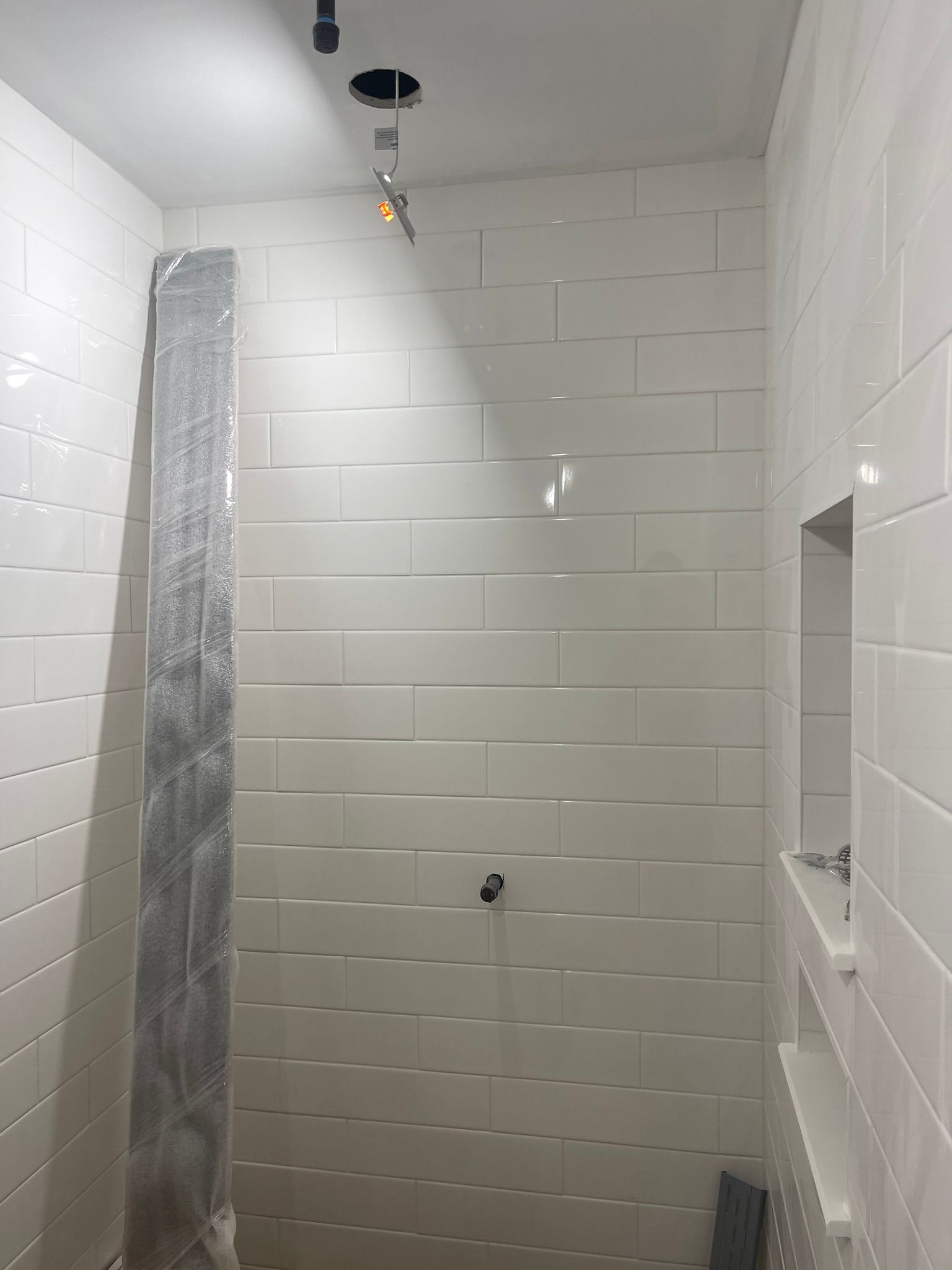 A shower interior featuring white subway tiles, a recessed shelf, and an unfinished plumbing fixture in the ceiling.