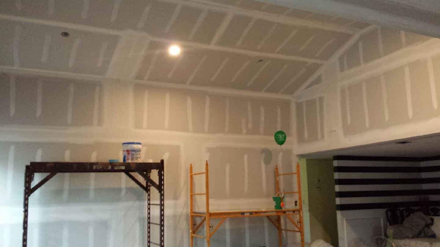 Interior view of a room under renovation with bare drywall, taped seams, and scaffolding against the walls.