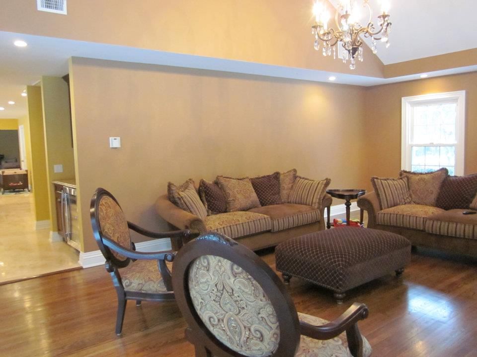 A living room with brown walls, a matching sofa and chairs, an ottoman, a chandelier, and wood flooring.