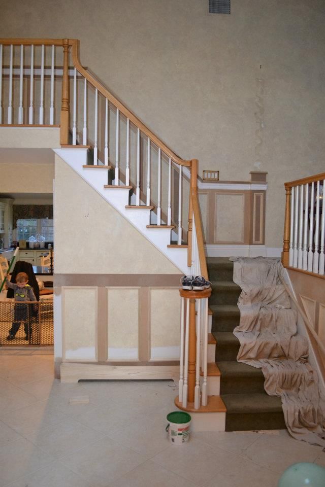 A staircase in a room under renovation, featuring unfinished wooden trim, wall paneling, and a drop cloth on the steps.
