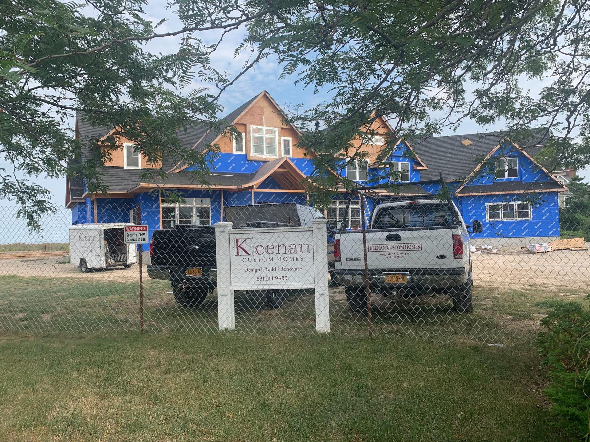 A partially built house under construction with blue protective sheathing and a project sign in the foreground.