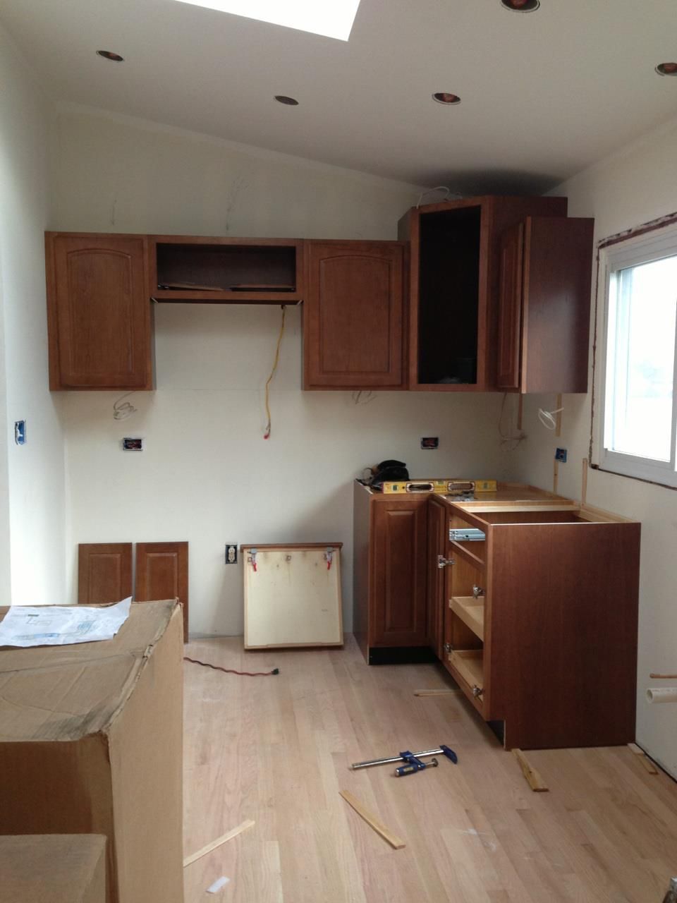 A partially installed kitchen with wood cabinets, light-colored walls, and unfinished flooring under recessed lighting.