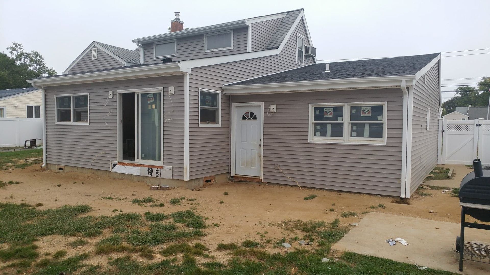 The rear view of a two-story house with beige siding, a sliding glass door, a side entrance, and an unfinished yard.