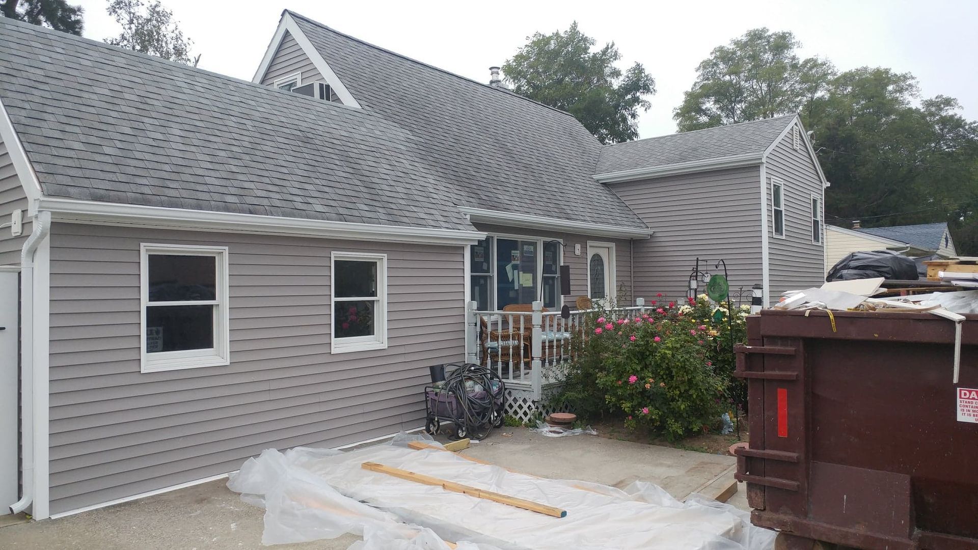 A single-story grey house with white trim and a dumpster in the front yard during a renovation.