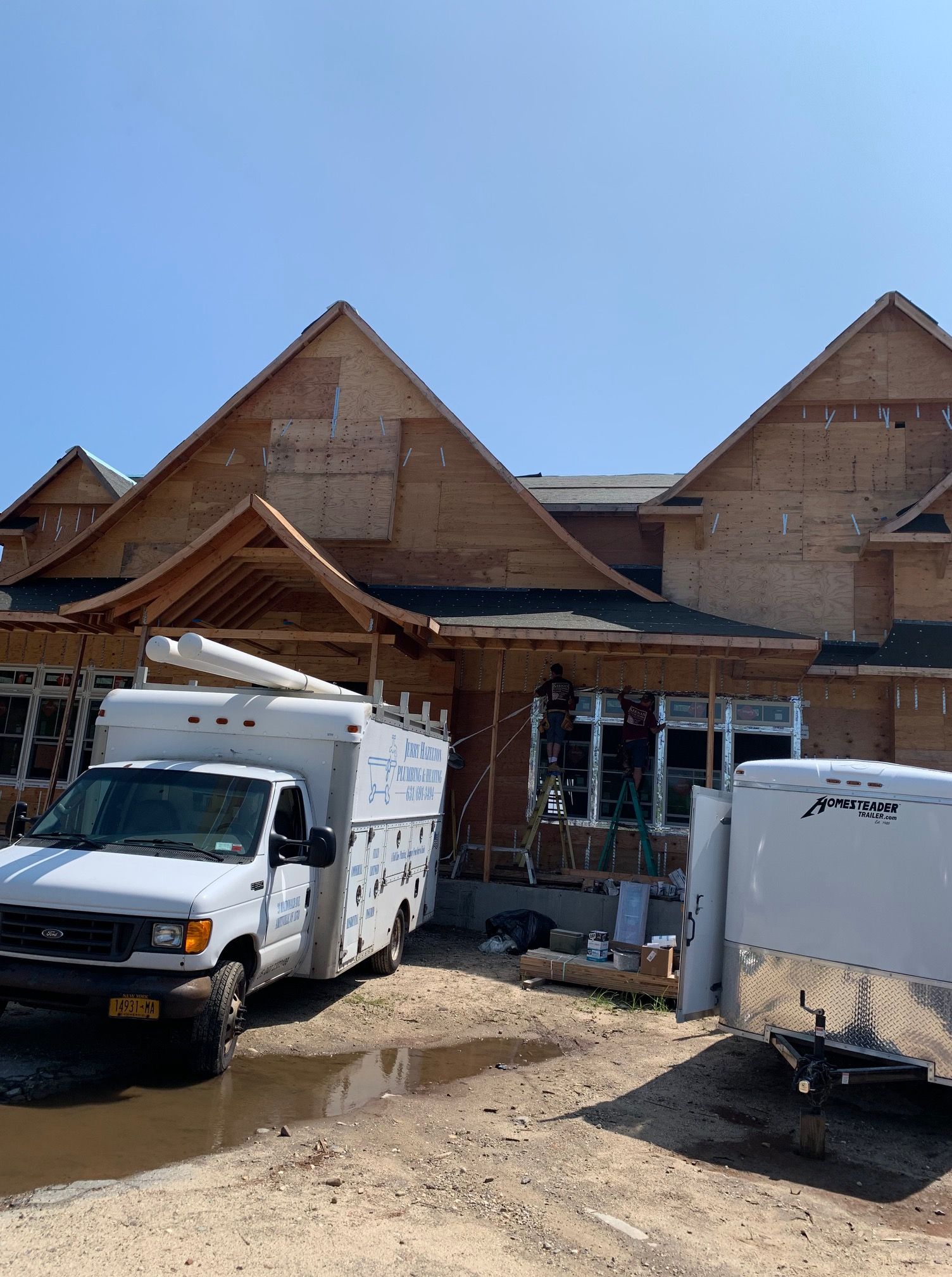 A construction site with two work trucks parked in front of a wooden, multi-gabled house under construction.