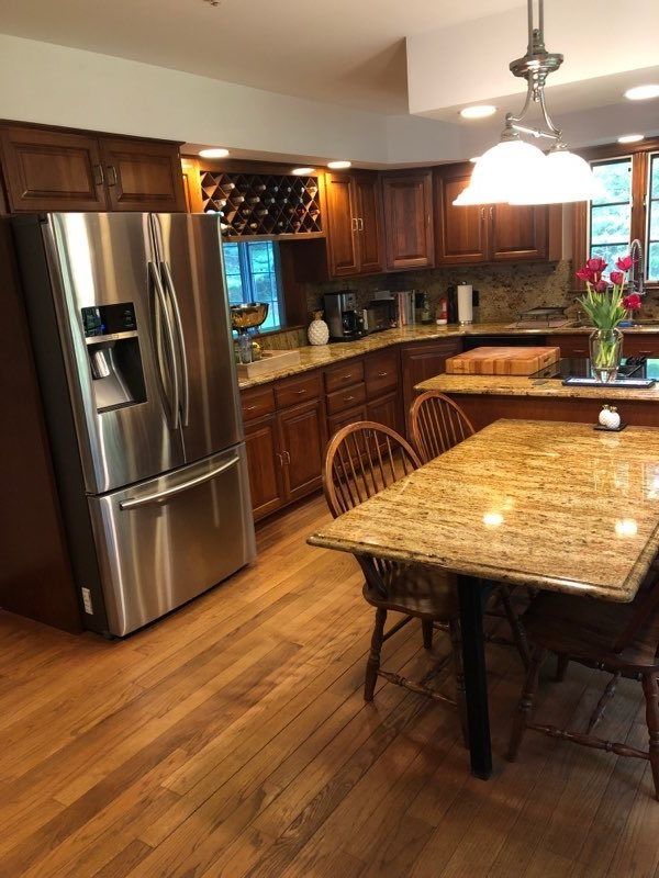A kitchen with wooden cabinets, a stainless steel refrigerator, granite countertops, and a dining table with chairs.