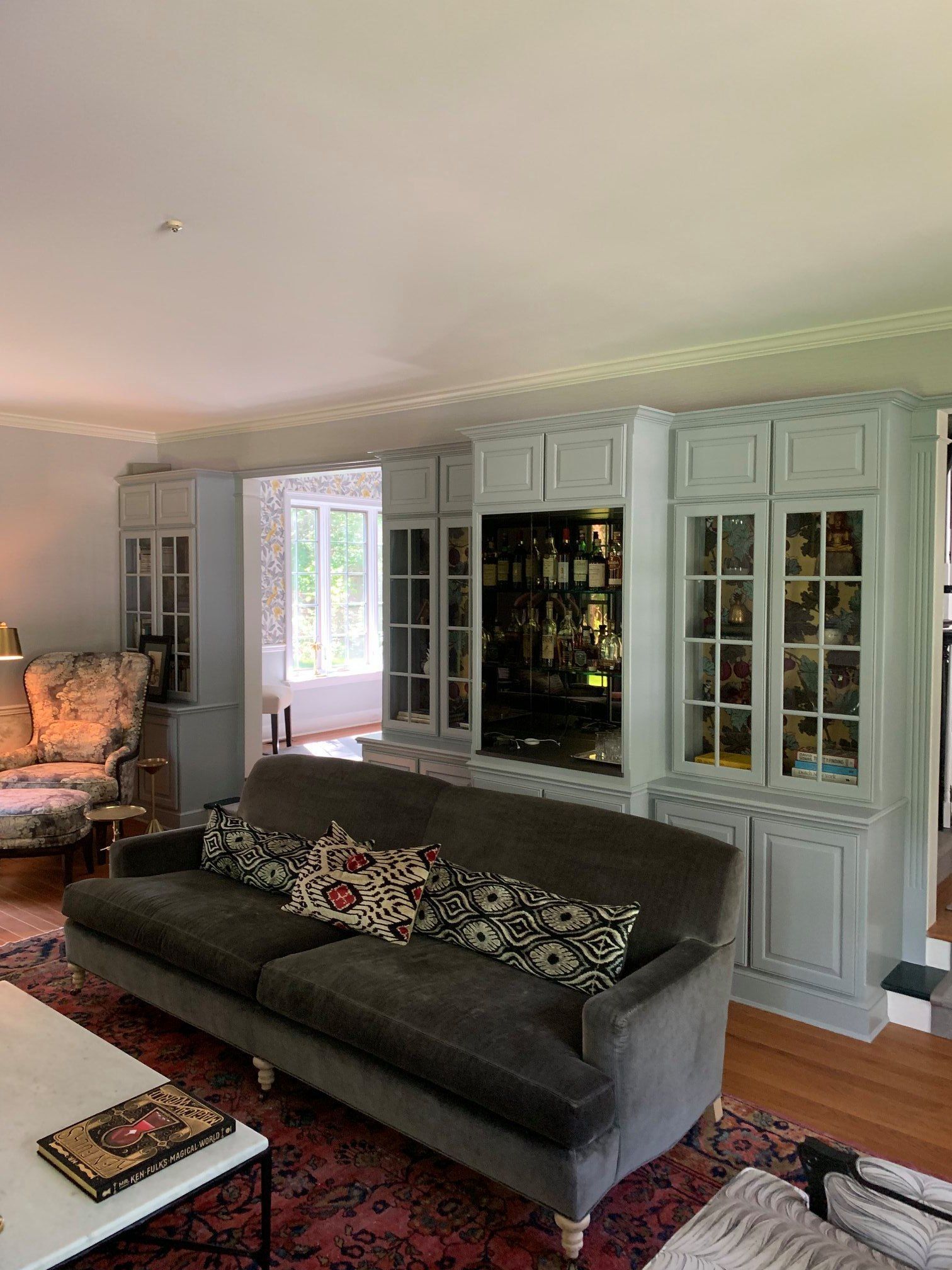 A grey sofa faces a large, light-blue built-in storage unit with glass-front cabinets and a dark-toned bar display.