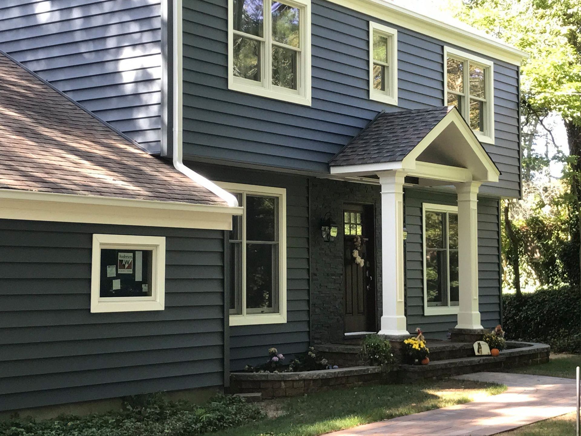 A two-story blue-gray house with a white-pillared entryway, a brick foundation, and a stone walkway.