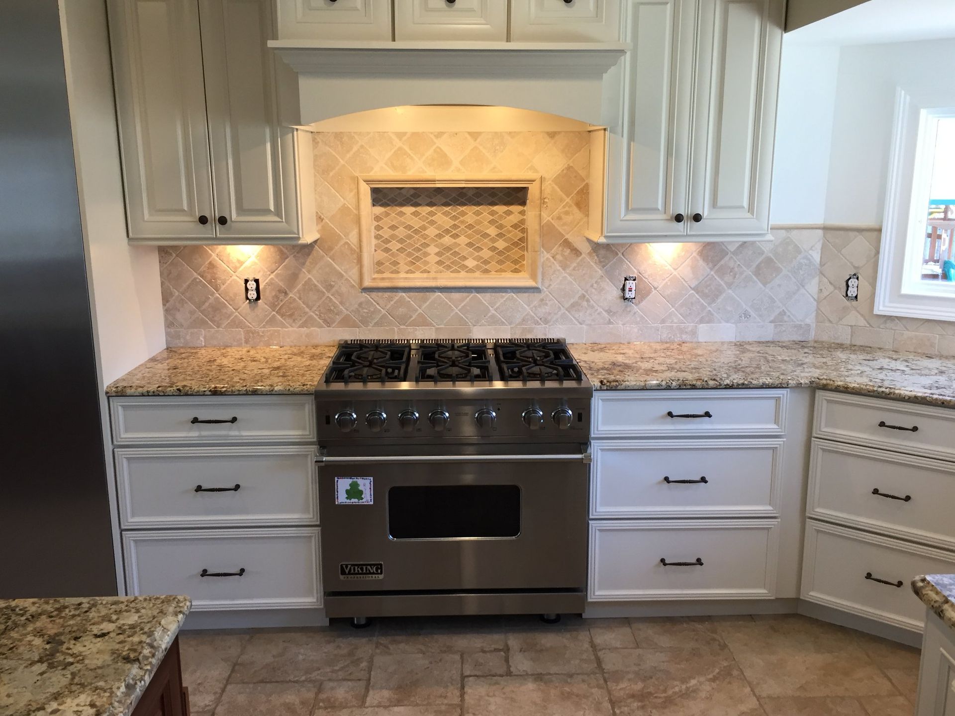 A stainless steel Viking stove sits between white cabinets and a light granite countertop with a tiled backsplash.